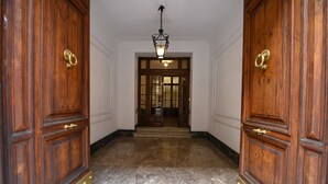 A hallway with wooden doors and a marble floor leading to a room with a large window and a chandelier. - Three Steps from Spanish Steps (Roma)