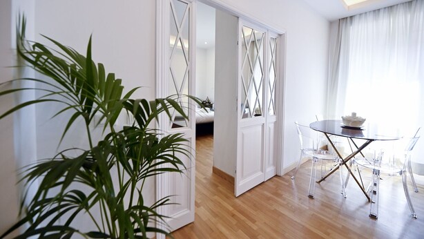 A modern room with a wooden floor, white walls, and a dining area with a glass table and chairs. - Three Steps from Spanish Steps (Roma)