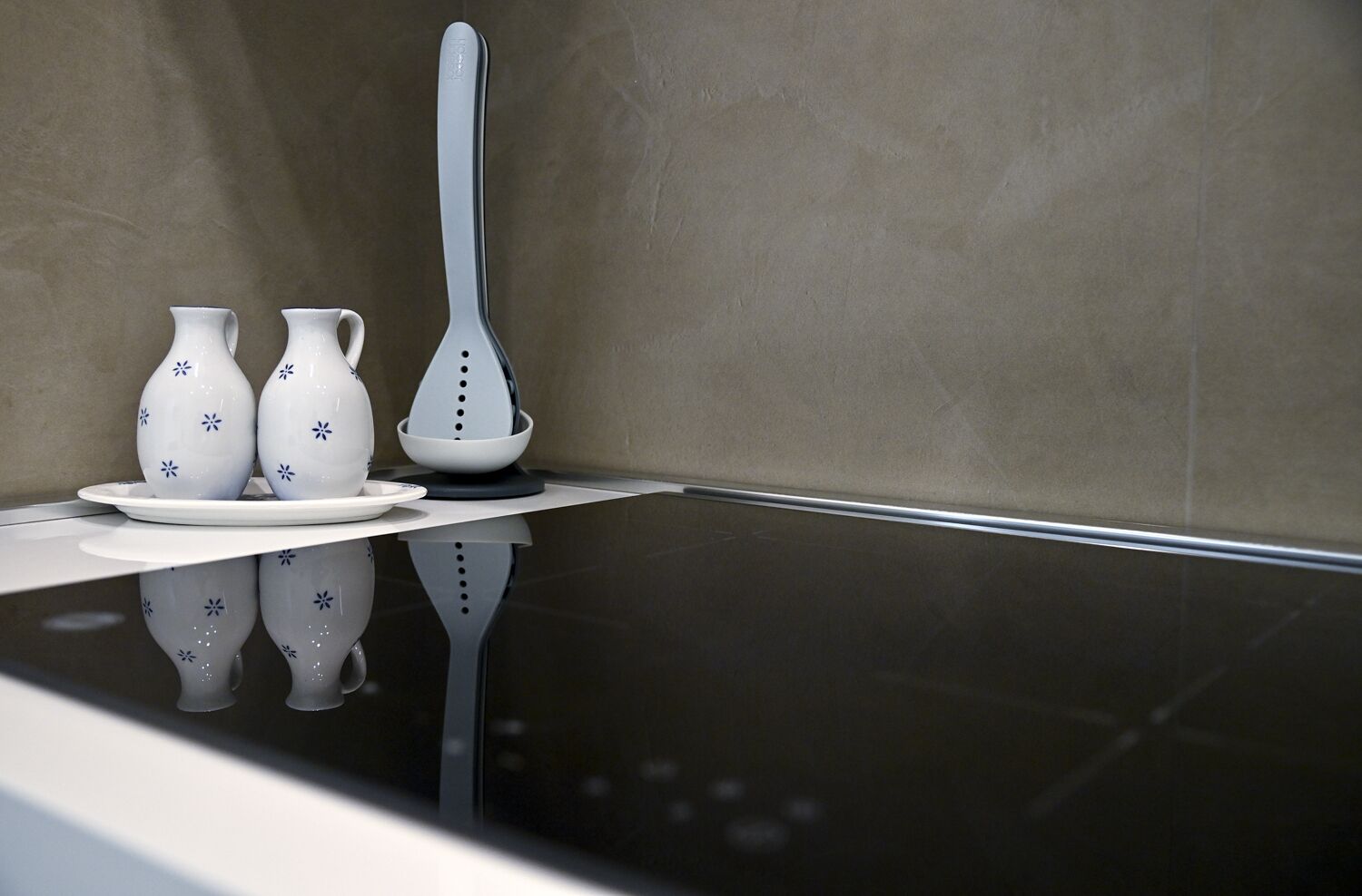 Une cuisine moderne avec un plan de travail noir brillant, une assiette blanche, deux vases blancs ornés de motifs bleus et une théière blanche.
