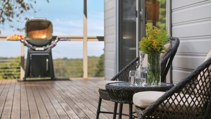 Una terraza de madera con una parrilla y una mesa con un florero y vasos.