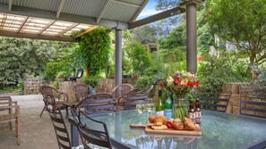 Un patio al aire libre con una mesa de vidrio, sillas de mimbre y una variedad de comida y bebidas.
