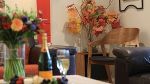 Ein Essbereich mit Tisch für zwei Personen, mit einer Champagnerflasche, einem Glas und einer Vase mit Herbstlaub.