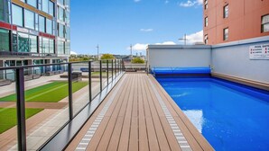 Area piscina con un pontile in legno, ringhiera in vetro e cartello con le norme di sicurezza.