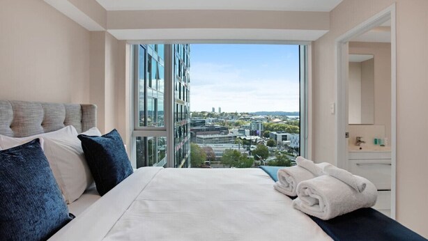 Una camera d'albergo moderna con un letto grande, vista sulla città e bagno parzialmente visibile da una porta aperta.