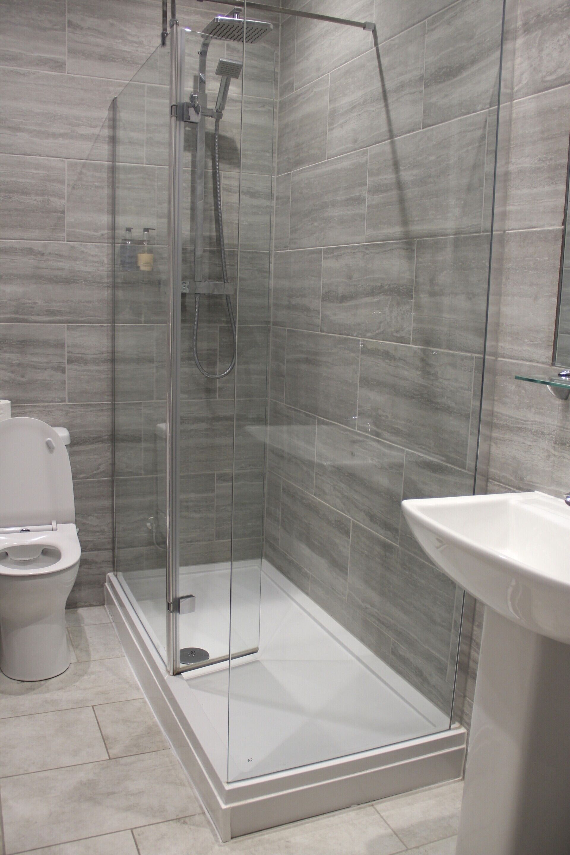 A modern bathroom with a glass-enclosed shower, a white toilet, and a pedestal sink.