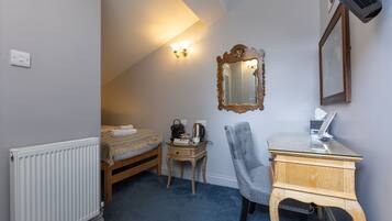 A small bedroom with a bed, a wooden nightstand, a chair, a desk with a laptop, a mirror, and a radiator.