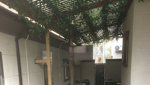An outdoor patio area with artificial grass, wicker furniture, and a pergola with hanging plants. - Downunder Suites (Abuja)