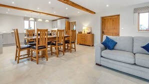 A spacious living area with a dining table, wooden chairs, a grey sofa, and a wooden cabinet.