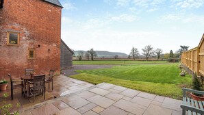 A brick building with a patio area, a lawn, and a view of the countryside.