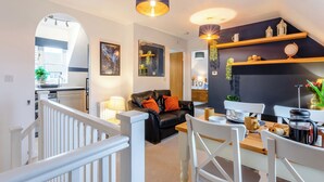 A modern living room with a black leather sofa, white chairs, and a dining table. There are pendant lights, a black accent wall, and a view into the kitchen. - Delightful recently completed Annexe close to Cambridge. (Cambridge)