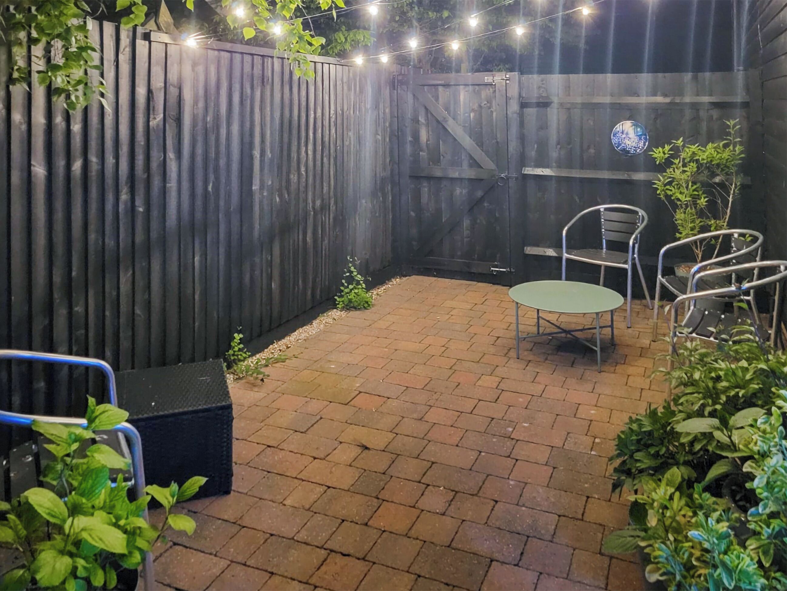 Un patio con piso de ladrillo, cerca de madera y una mesa con sillas.