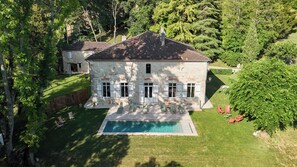 Una casa grande con piscina, rodeada de abundante vegetación y árboles.