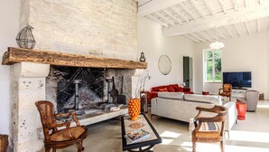 A living room with a stone fireplace, wooden furniture, and a television. - LA Maison DE Ninette (Castelculier)