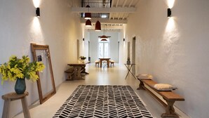 A hallway with a patterned rug, a wooden bench, a table with chairs, and a tripod with a light. - LA Maison DE Ninette (Castelculier)