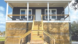 A two-story building with a wooden deck and a staircase leading to the upper floor. - Beautiful Beach Views Sleeps 8 (Gulfport)