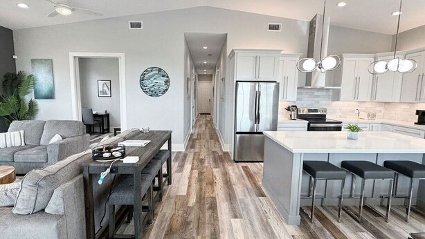A modern kitchen with a central island, bar stools, and a dining area with a sofa and coffee table. - Beautiful Beach Views Sleeps 8 (Gulfport)