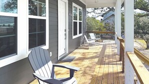 A covered porch with a wooden deck, white railings, and two Adirondack chairs. - Beautiful Beach Views Sleeps 8 (Gulfport)
