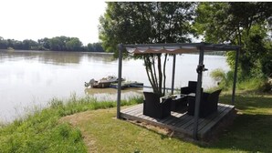 A wooden deck with outdoor seating and a pergola overlooking a lake. - Coin de Paradis en Bord de Dordogne 4 (La Riviere)
