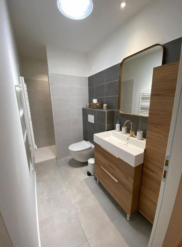 A modern bathroom with a white toilet, a wooden vanity with a mirror, and a shower area.
