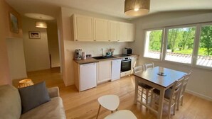 Une cuisine compacte avec des meubles blancs, une table à manger avec des chaises et une grande fenêtre offrant une vue sur la verdure.