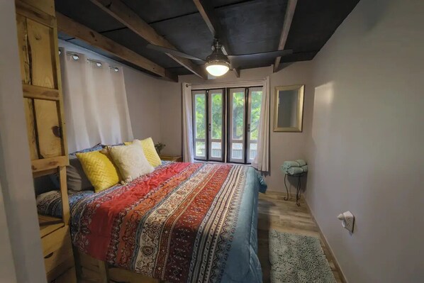 Een slaapkamer met een bed, een houten ladder, een raam met gordijnen en een plafondventilator.