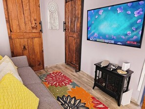 A room with a bed, a television mounted on the wall, a small table with a decorative item, and a colorful rug.