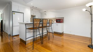 A modern kitchen with white cabinets, a wooden dining table with four chairs, a microwave, and a floor lamp.