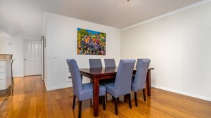 A dining area with a wooden table and six chairs, a colorful painting on the wall, and a white door in the background.