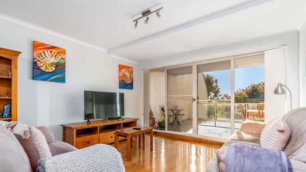 A living room with a flat-screen TV, wooden furniture, and a balcony with a table and chairs.