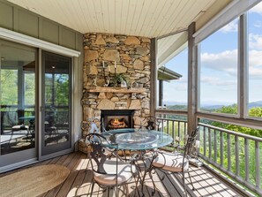 A stone fireplace, a glass table, and outdoor seating on a wooden deck.