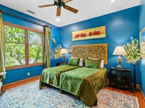 A bedroom with a large bed, two bedside tables, a ceiling fan, and a window with curtains.