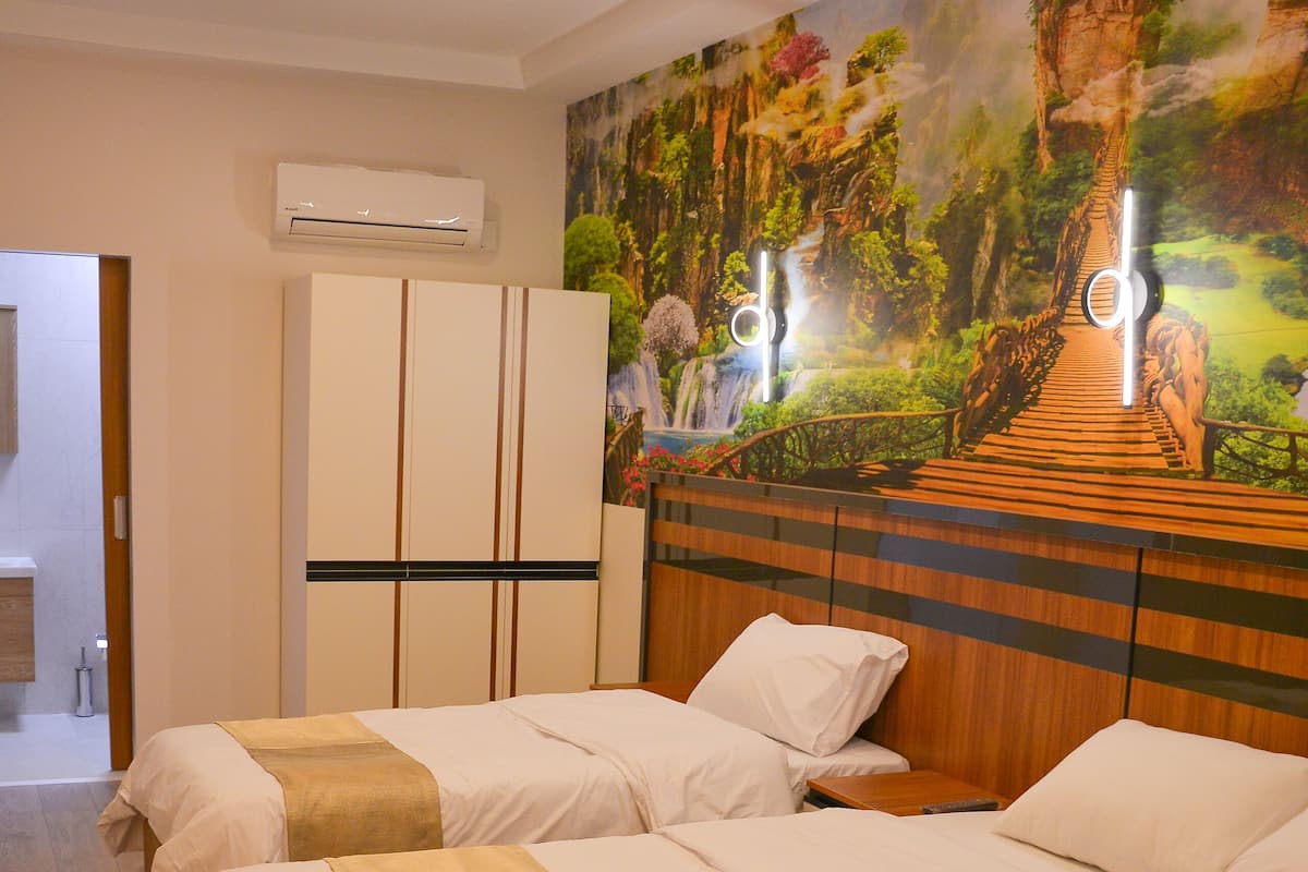 Habitación de hotel con dos camas, un mural grande en la pared, un equipo de aire acondicionado y suelo de madera.