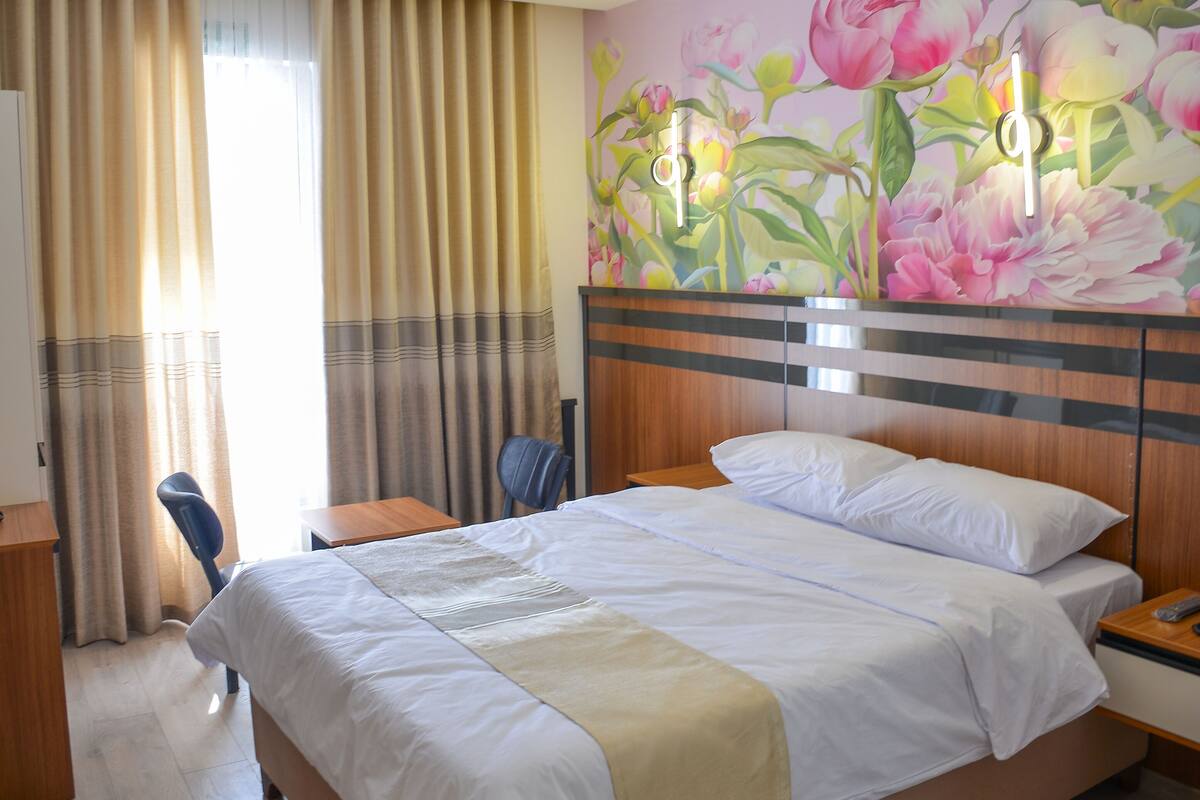 Habitación de hotel con cama, escritorio, silla y una pared decorada con un mural floral.