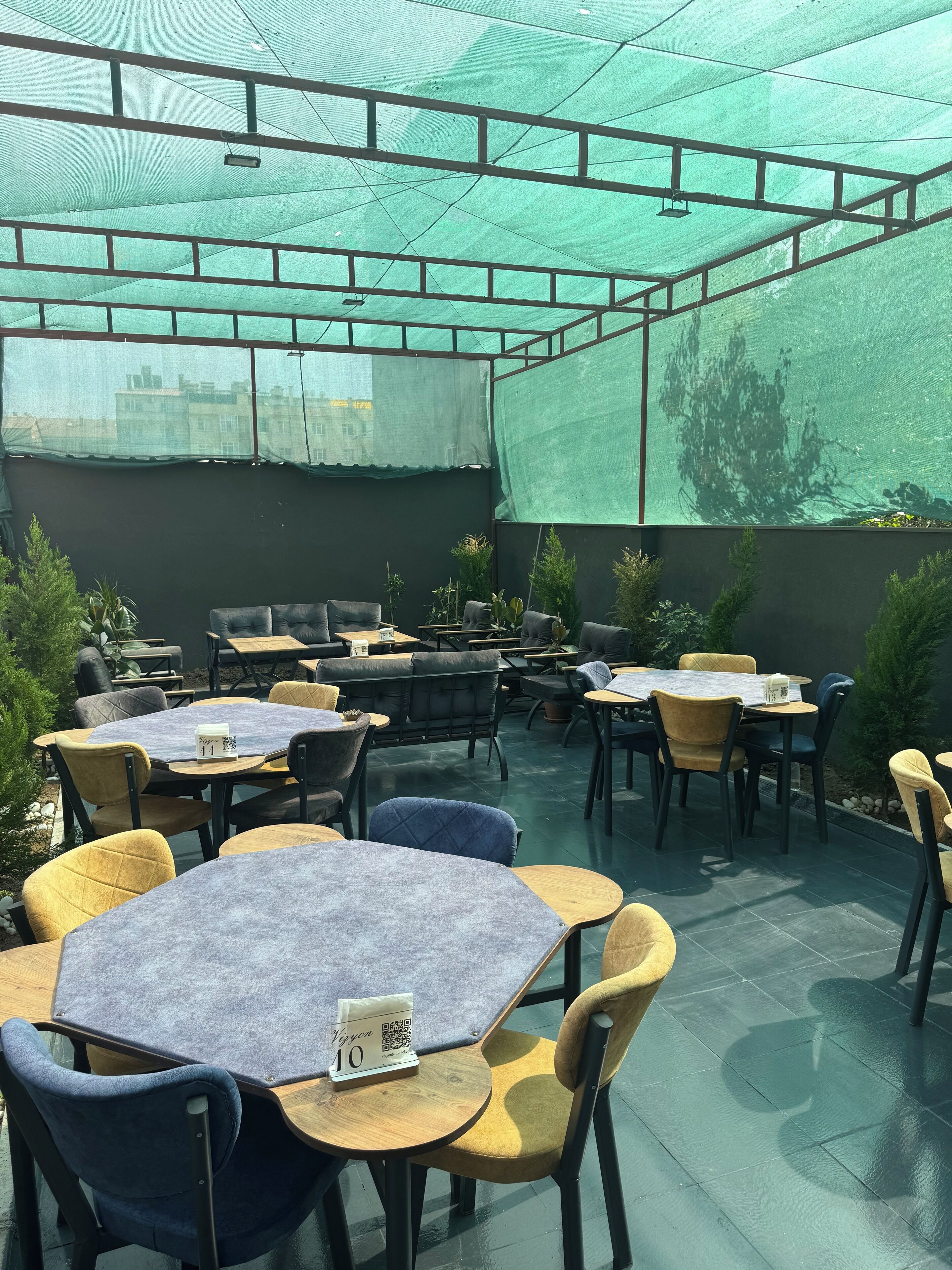 A covered outdoor seating area with tables and chairs, a QR code on a table, and a view of buildings in the background.