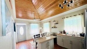 Una cucina con soffitto in legno, mobili bianchi, un tavolo da pranzo e una finestra con tende.
