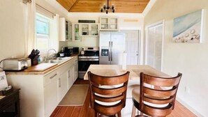 Una cucina con soffitto in legno, mobili bianchi, un tavolo da pranzo con sedie e un frigorifero.