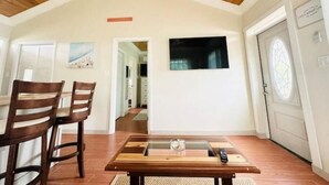 Zona pranzo con soffitto in legno, tavolo con sedie e TV a parete.