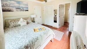 Una camera da letto con un letto, una ventola a soffitto, un quadro e una porta che dà su un'altra stanza.