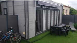 Une terrasse avec une table et des chaises, un vélo et un espace abrité avec des fenêtres.