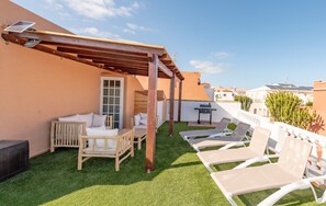 Eine Dachterrasse mit Kunstgrasanlage, Holzmöbeln und weißen Liegestühlen.