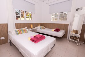 Ein Zimmer mit zwei Betten, einem kleinen Tisch und einem Fenster mit Blick auf Grünfläche.