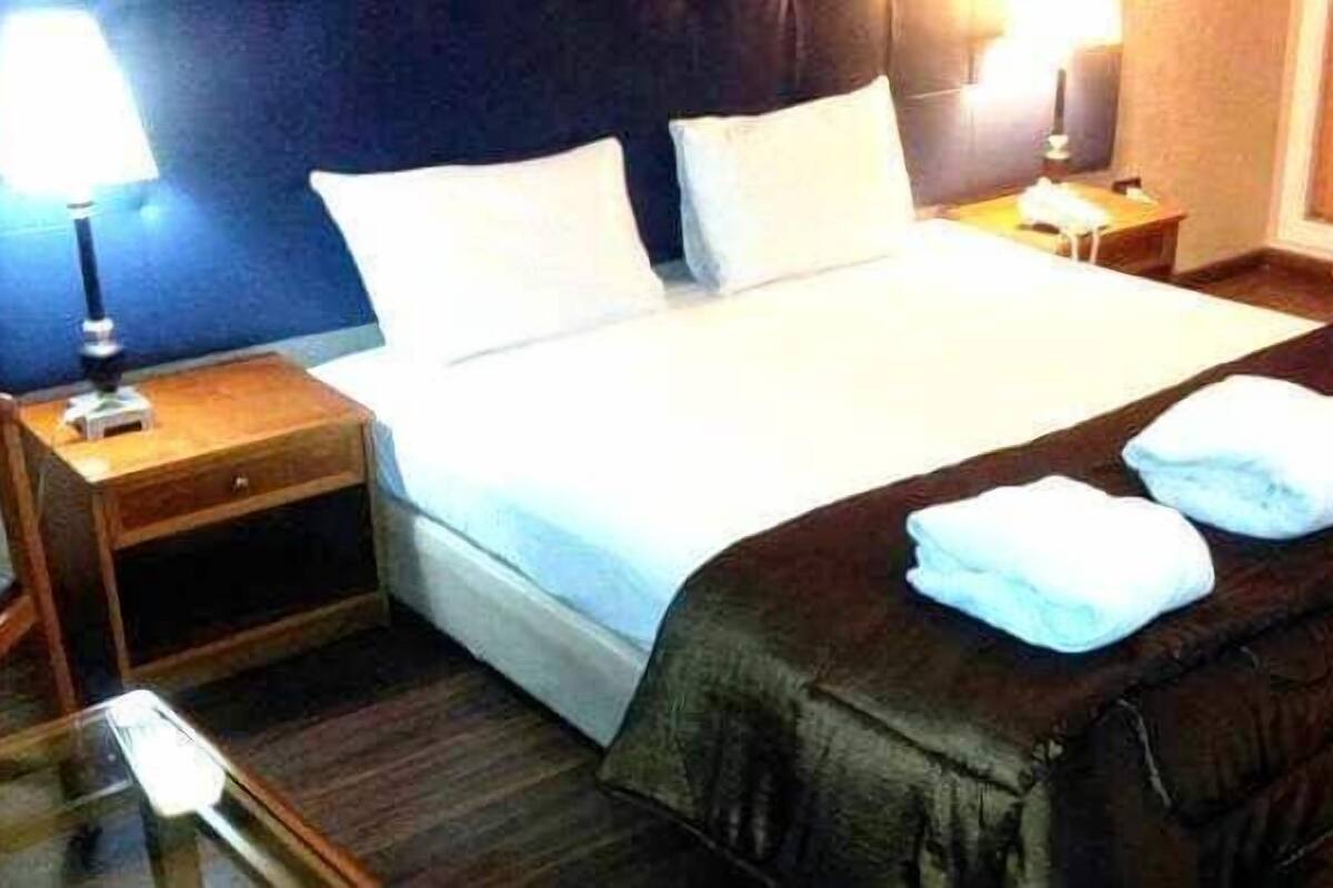 A hotel room with a large bed, two bedside tables, a nightstand, and a lamp.