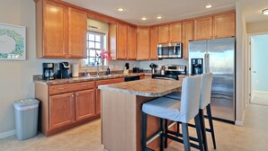 Una cocina moderna con armarios de madera, electrodomésticos de acero inoxidable, encimera de granito y una zona de bar con taburetes.