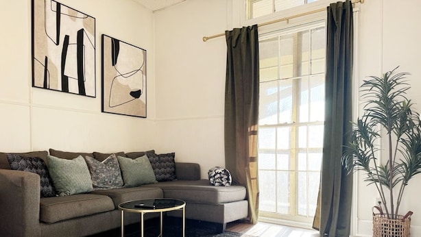 Ein modernes Wohnzimmer mit einem Ecksofa, einem Couchtisch und einem großen Fenster mit Vorhängen.