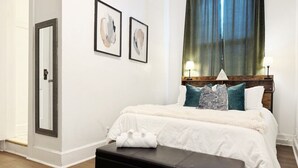 Ein Schlafzimmer mit Bett, einer Bank, einem Spiegel und Bildern an der Wand.