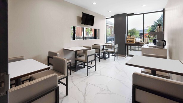 A modern cafe with multiple seating areas, a flat-screen TV mounted on the wall, and large windows offering a view of the street. - Days Inn By Wyndham Staten Island (Staten Island)