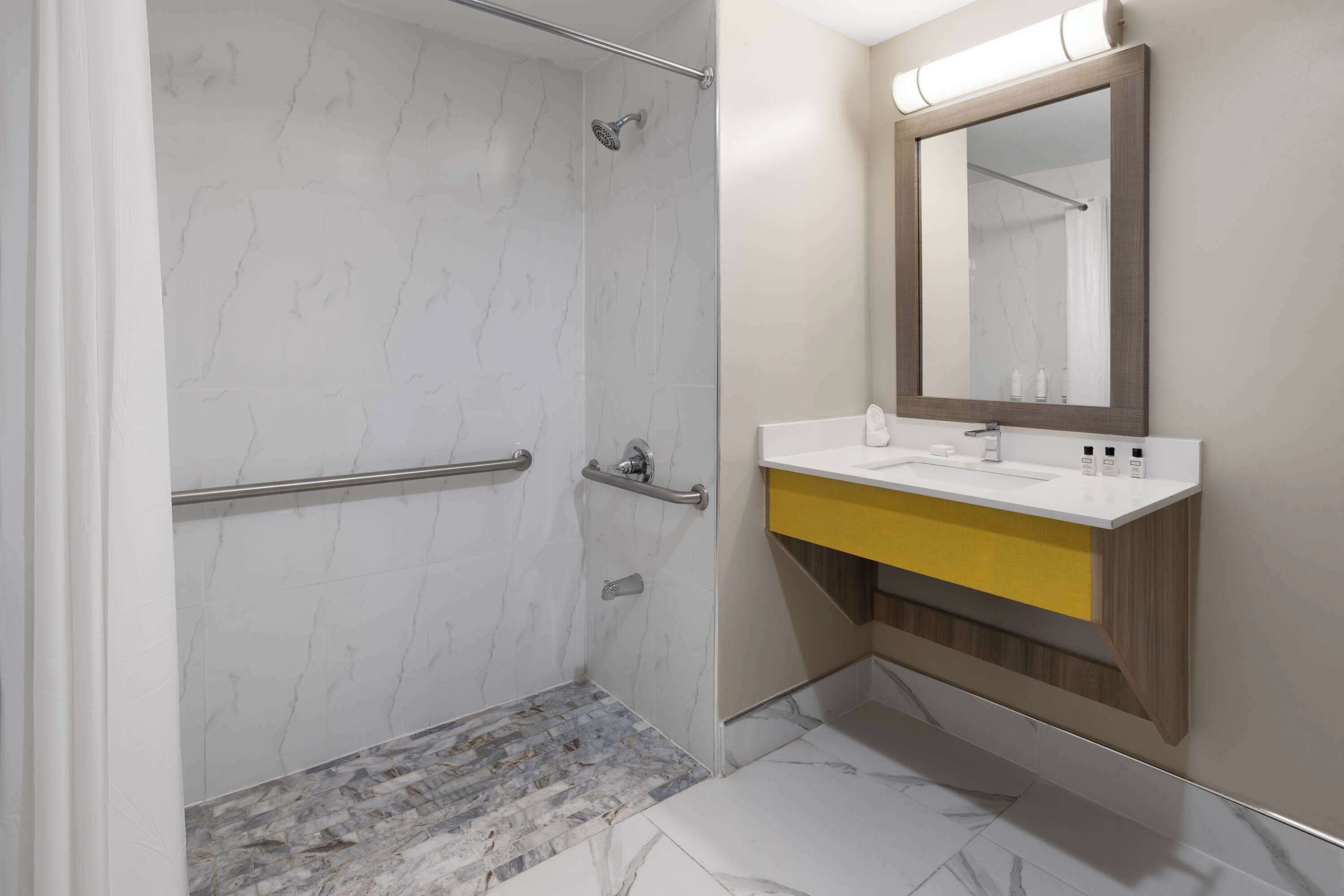 Un baño moderno con ducha, lavabo con espejo y una pared de acento amarilla.
