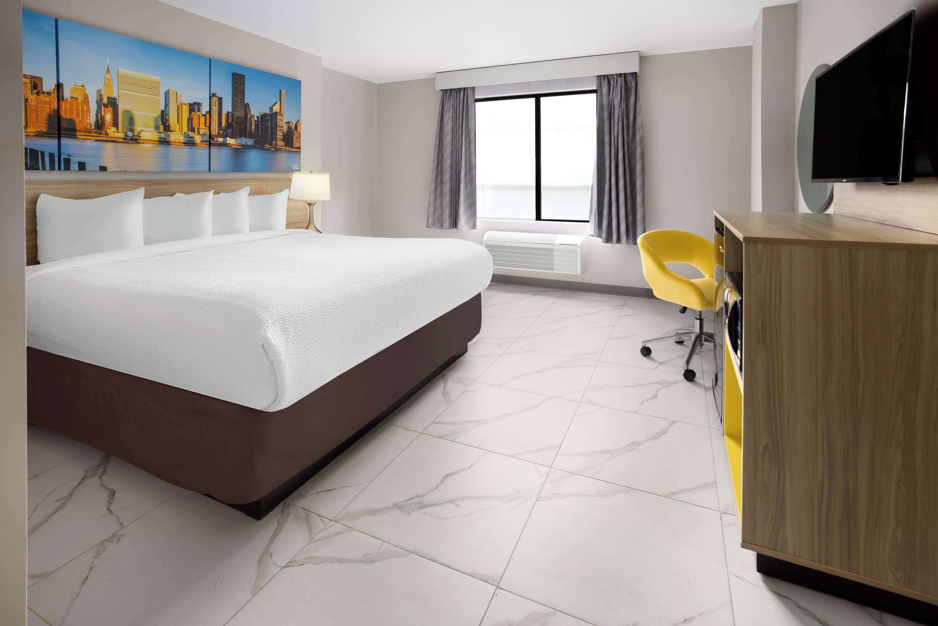 A hotel room with a large bed, a desk with a chair, a flat-screen TV, a painting of a cityscape, and a window with curtains.