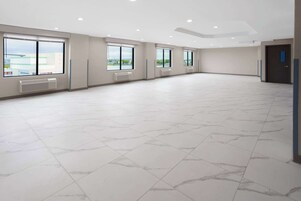 Una habitación amplia y luminosa, con grandes ventanales, suelo de baldosas y una puerta.