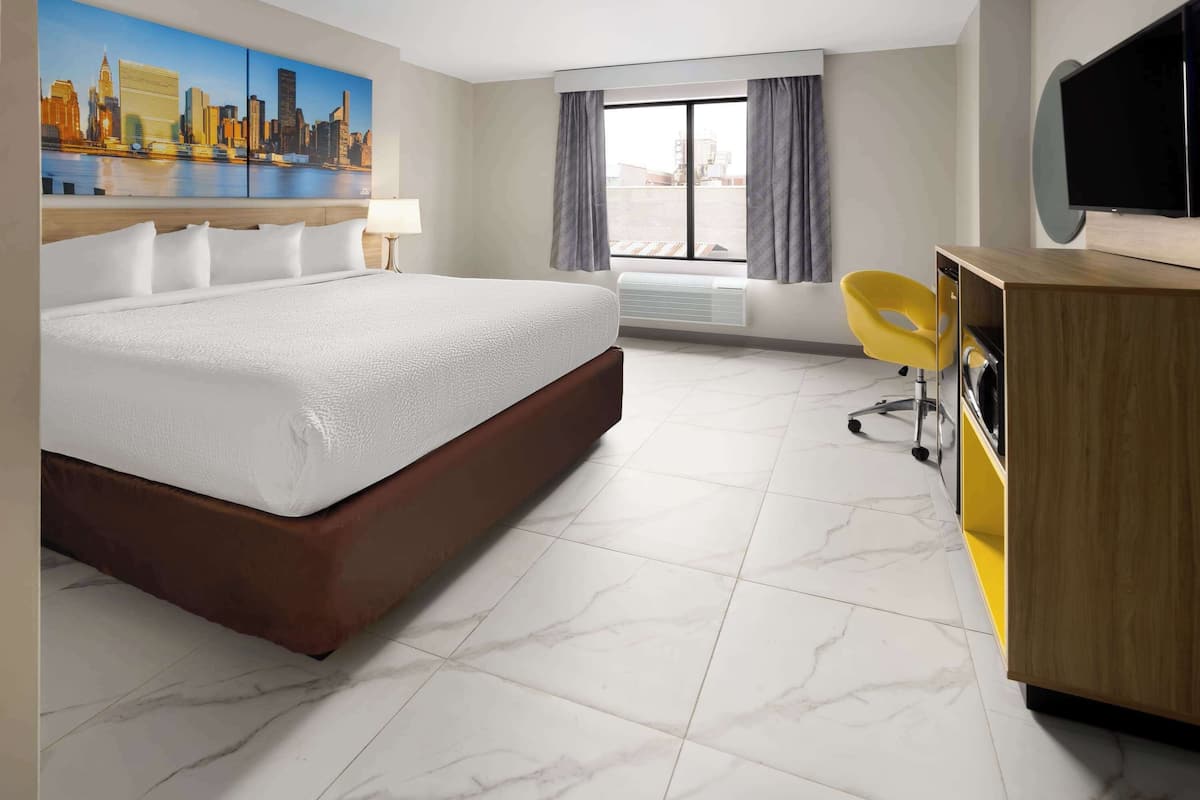 A hotel room with a large bed, a desk with a chair, a flat-screen TV, and a window with curtains.